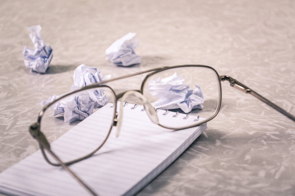 Close-Up Photography of Eyeglasses Near Crumpled Papers